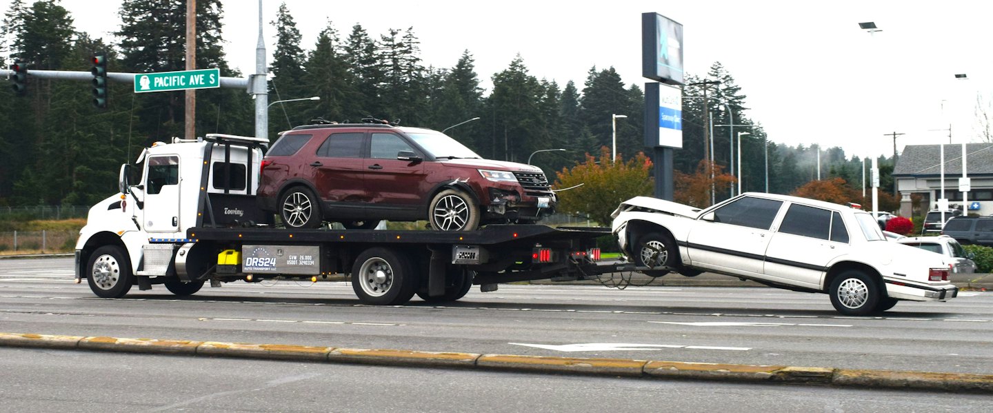 Tow truck carries damaged SUV and sedan on a cloudy day.